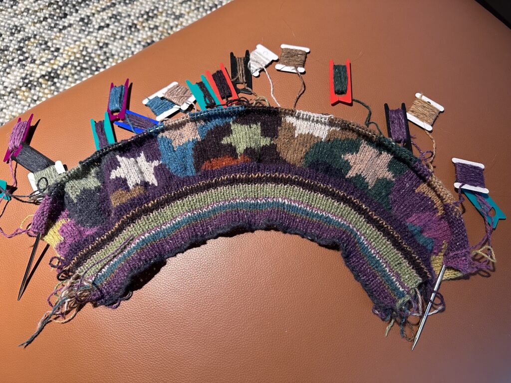 An in-progress intarsia knitted sweater with swirls and stars in many colours