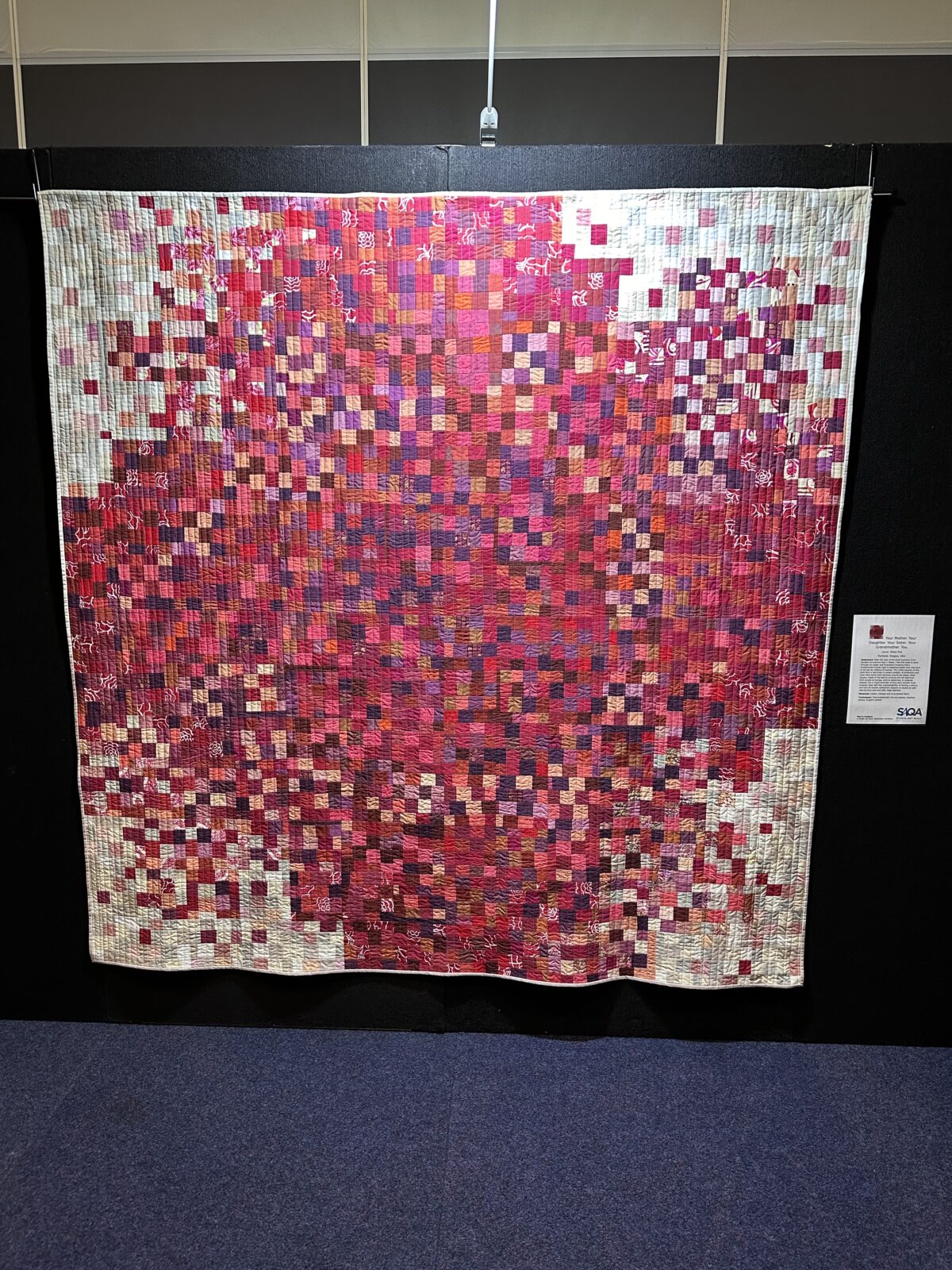 A quilt made up of hundreds of red squares making an abstract red cross