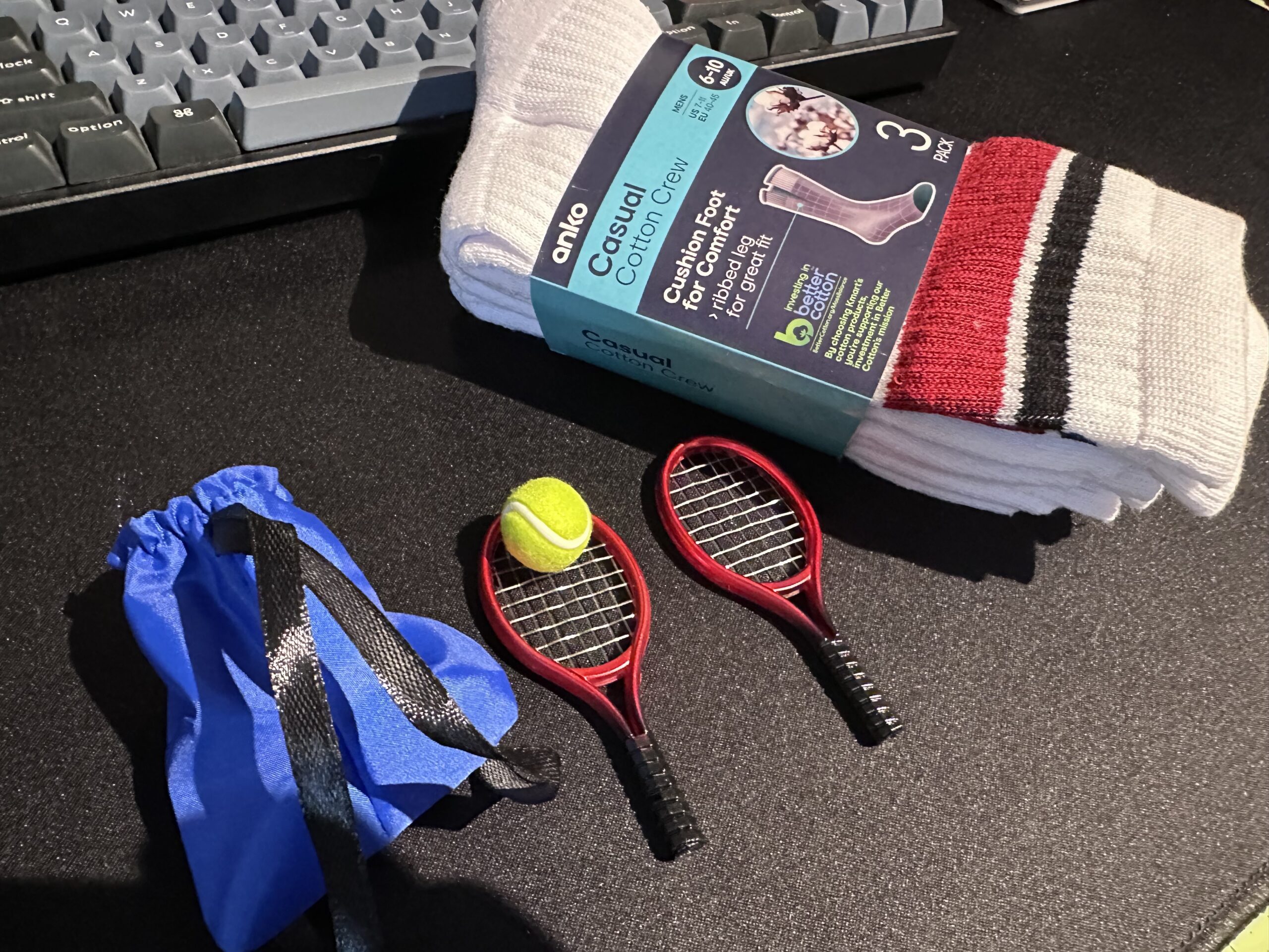 A pack of men’s athletic tube socks next to two miniature tennis rackets with a ball and a racket bag