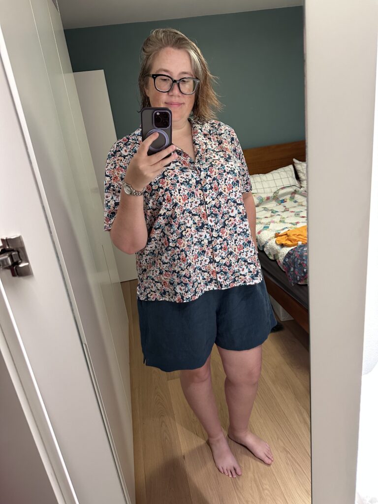 A selfie of a woman in blue linen shorts with a printed button-down short-sleeved shirt