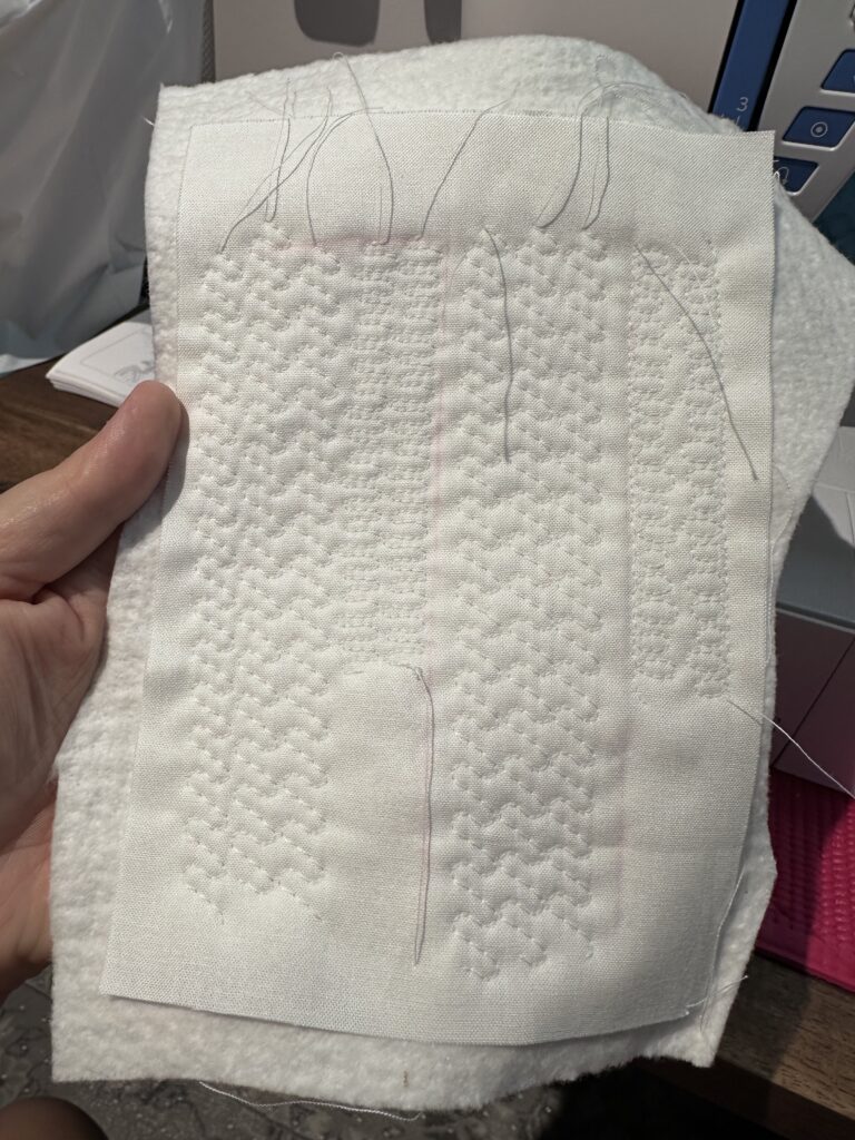 A swatch of white fabric, quilted with several different sewing stitch patterns