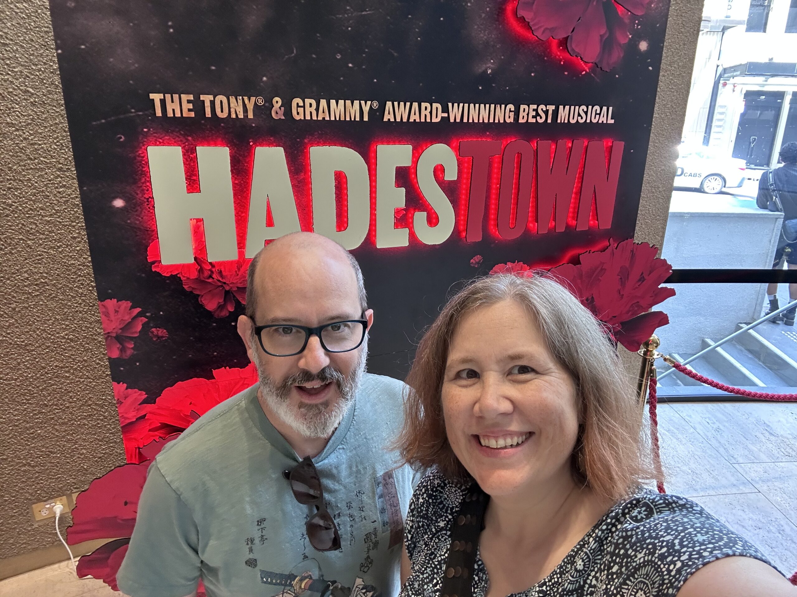 Two people in front of a sign for the musical Hadestown