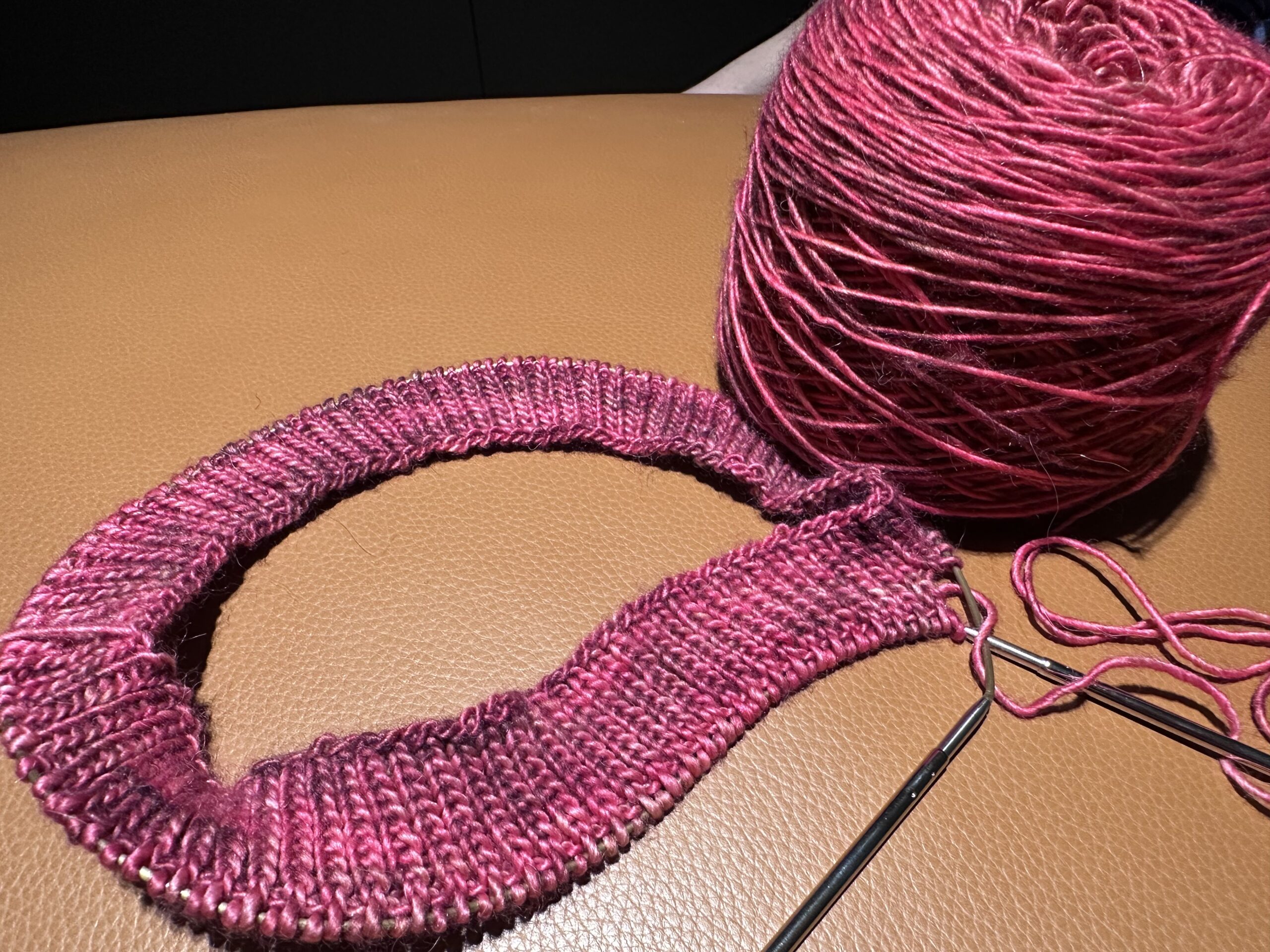 A cake of pink knitting wool next to a piece of circular knitting