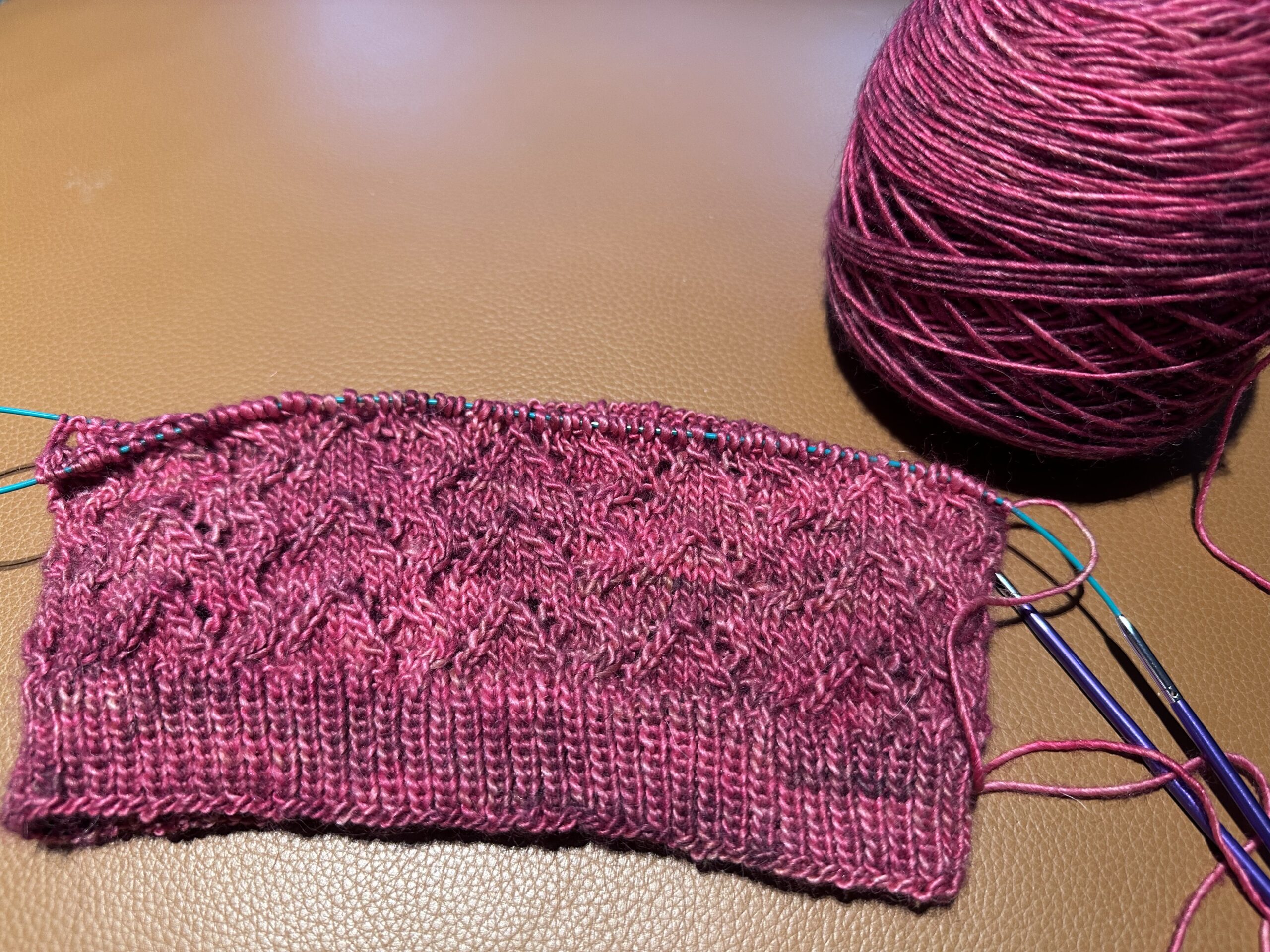 A ball of pink wool and a pink knitted cowl with cables and lace