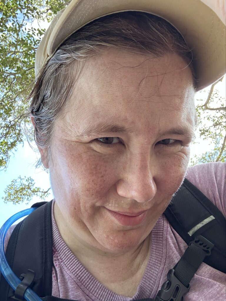 A very sweaty woman lifting up her cap to show a not-very-visible lump on her head