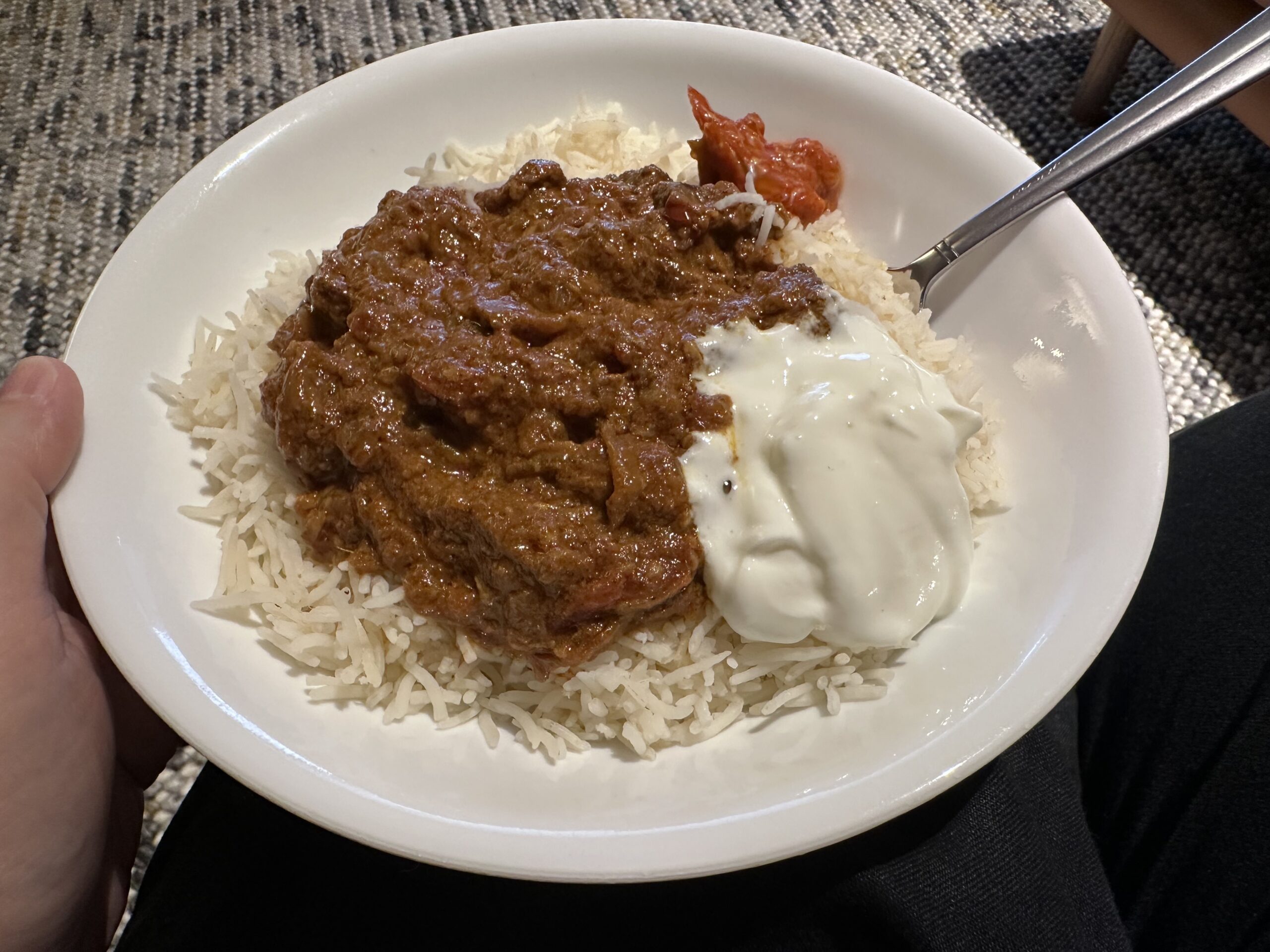 A bowl with rice, a meaty red curry, yogurt, and a bit of pickle